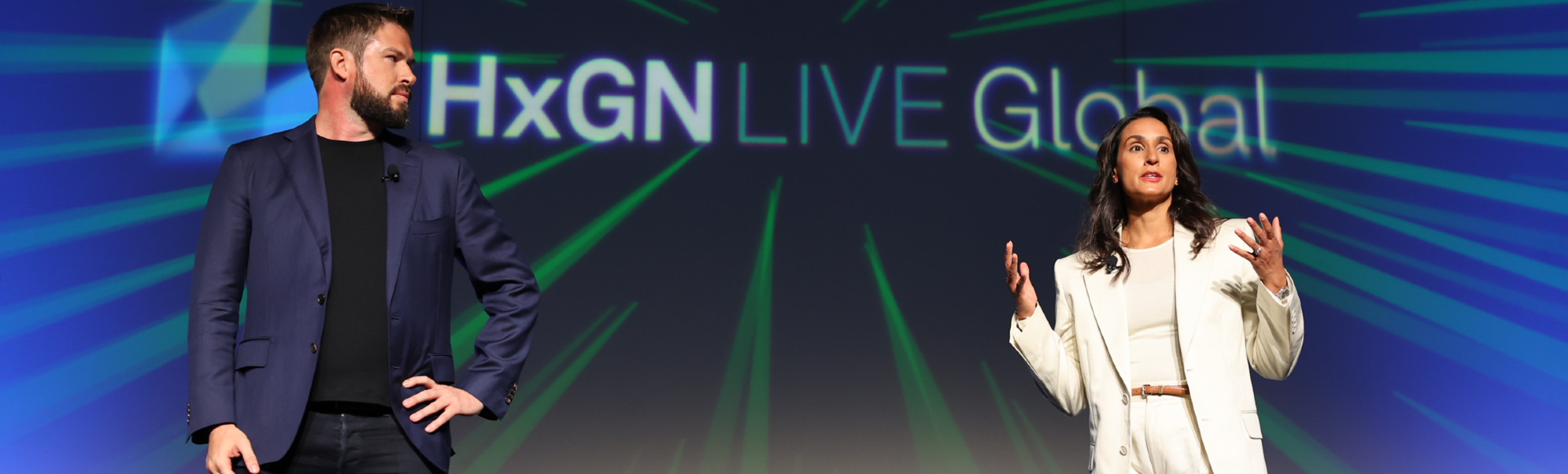 Keynote presenters speaking at HxGN LIVE Global 2023 in front of a blue and green banner.